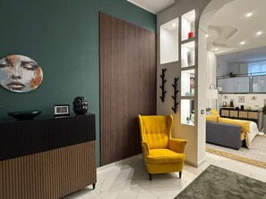 A modern living room with a yellow armchair, a wooden panel wall, and a kitchen visible through an open doorway. - ENTIRE APARTMENT IN DOWNTOWN NAPLES (Napoli)