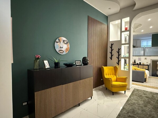 A modern reception area with a dark wood reception desk, a yellow armchair, and a large abstract painting on the wall. - ENTIRE APARTMENT IN DOWNTOWN NAPLES (Napoli)
