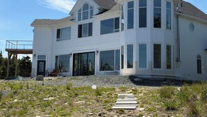 A large, multi-story white house with a prominent tower, large windows, and a gravel driveway.
