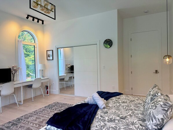 Un dormitorio con cama, escritorio, silla, ventana grande y puerta.