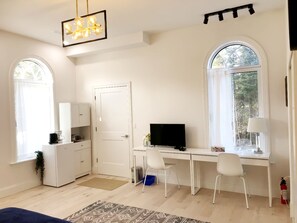 Una habitación con escritorio, dos sillas, televisor, armario blanco, cafetera y extintor.