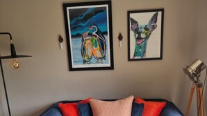En blå sofa med røde og mønstrede puder, et indrammet billede af fugle, en gulvlampe og en tripodal lampe.