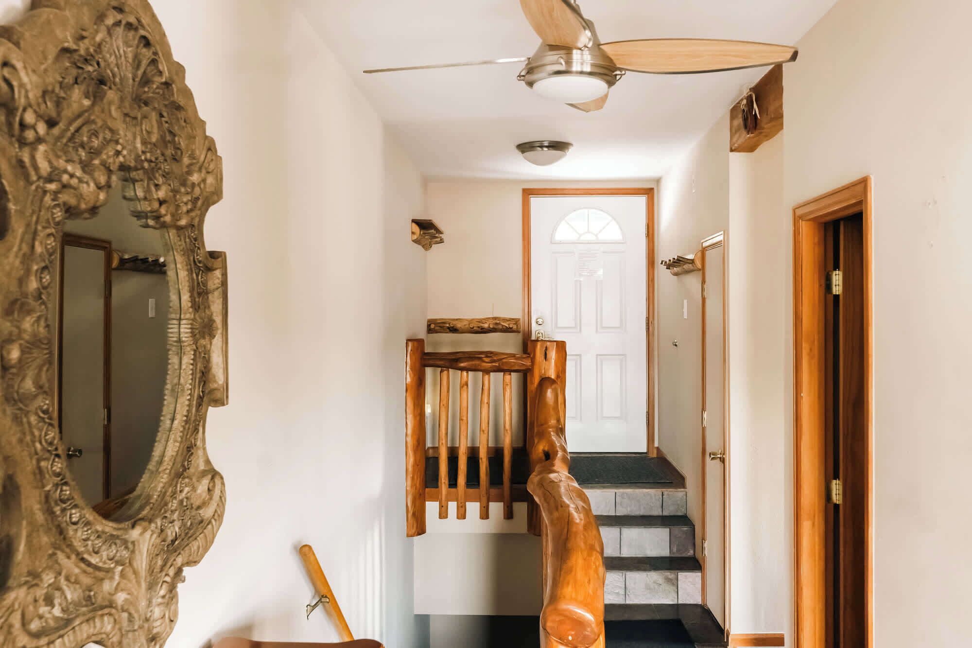 Un corridoio con una scala in legno, una ventola a soffitto e un grande specchio decorativo.