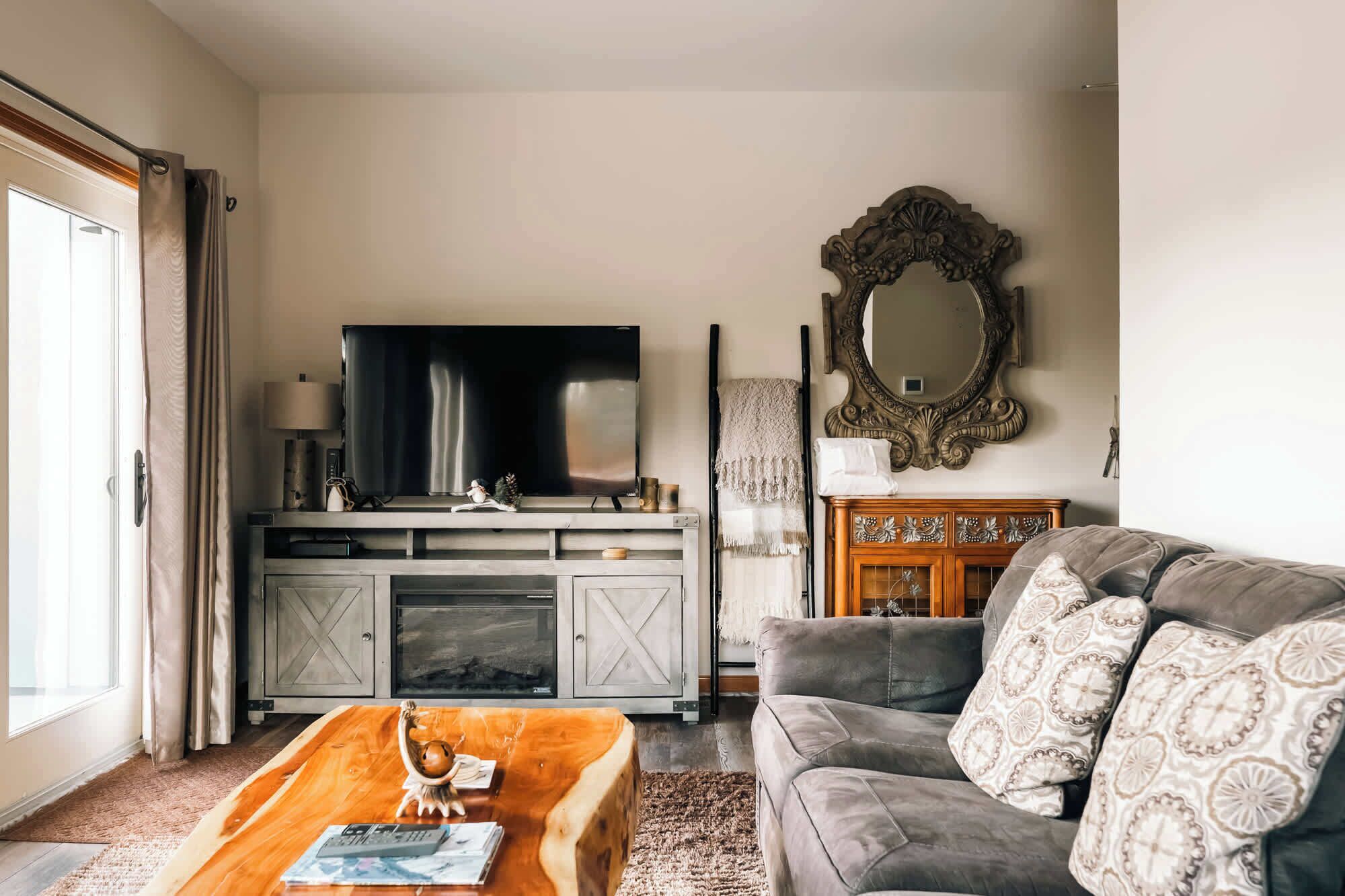 A living room with a television, sofa, coffee table, fireplace, and a mirror.