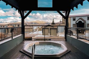 Un bain à remous sur une terrasse en bois, avec vue sur un quartier résidentiel et les montagnes.