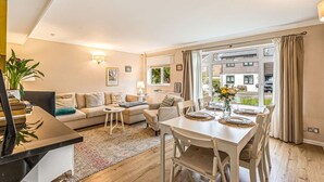 Ein modernes Wohnzimmer mit Sofa, Esstisch und Stühlen, einem kleinen Beistelltisch und Blick ins Freie.