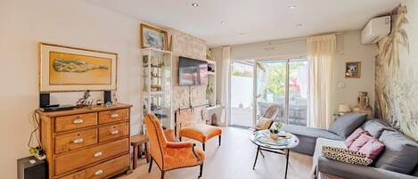 Ein Wohnzimmer mit Sofa, Sesseln, Hocker, Fernseher und einem Holzkasten.