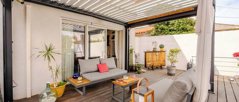 Une terrasse extérieure couverte, aménagée avec un canapé, une table et des plantes en pot.