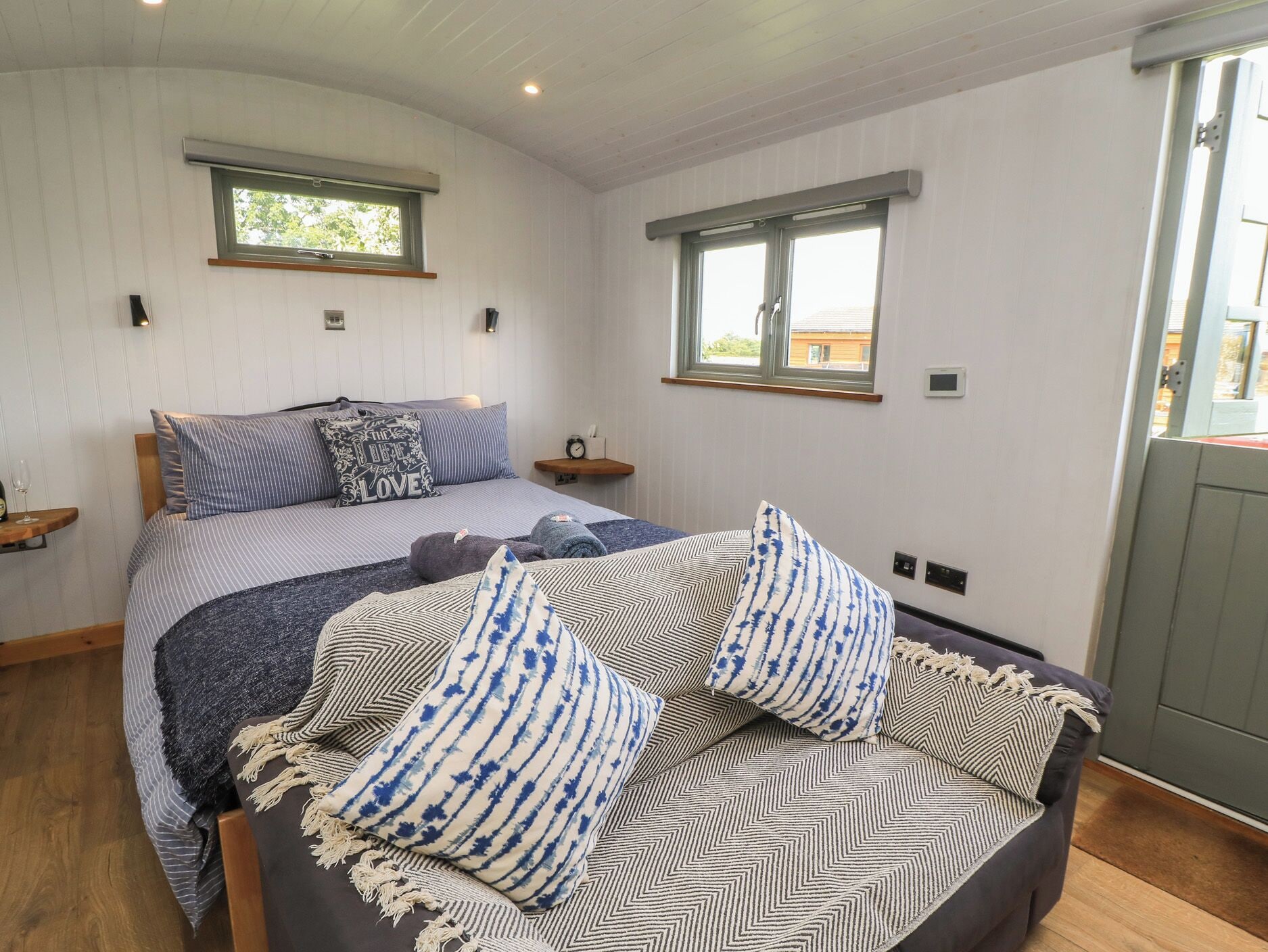 A bedroom with a bed, two windows, a bedside table, and a nightstand.