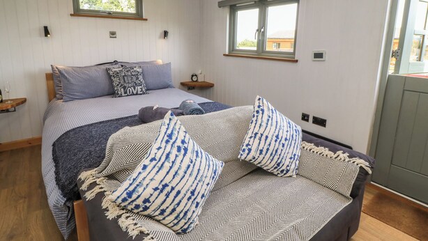 A bedroom with a bed, two windows, a bedside table, and a nightstand. - Damsons (Taunton)