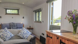 A cozy room with a sofa, a wooden cabinet, a window, and a small shelf. - Damsons (Taunton)