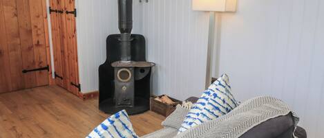Una habitación acogedora con una estufa de leña, un sofá con cojines estampados y una puerta de madera.