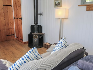 Ein gemütliches Zimmer mit Kaminofen, einer Couch mit gemusterten Kissen und einer Holztür.