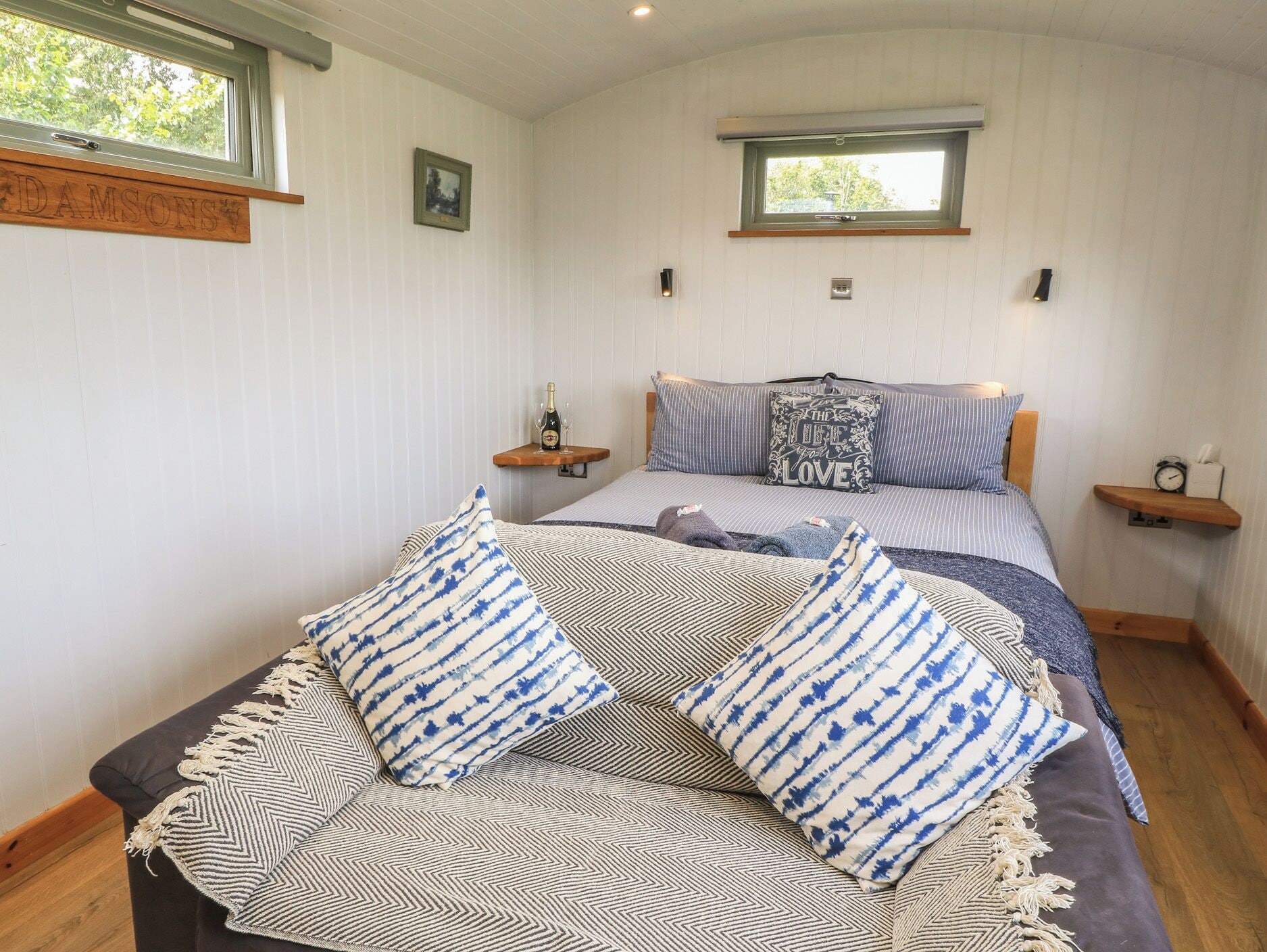 A bedroom with a bed, two bedside tables, a window, and a wall-mounted shelf.
