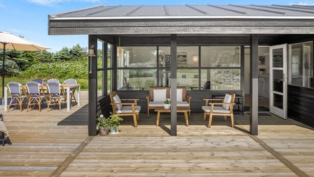 Un espacio de estar al aire libre cubierto con mobiliario de madera y grandes ventanales.