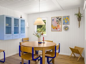 Un coin repas avec une table ronde en bois, des chaises bleues, une lampe suspendue et des œuvres d’art murales.