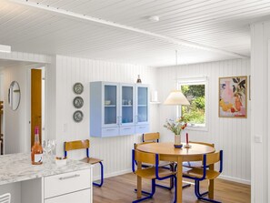 Een kamer met een houten eettafel, blauwe stoelen, een witte kast en een raam met uitzicht op groen.