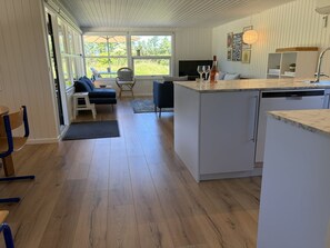 Eine moderne Küche mit integriertem Geschirrspüler, einem Essbereich mit Tisch und Stühlen sowie einer gemütlichen Sitzecke mit Sofa und Sesseln.