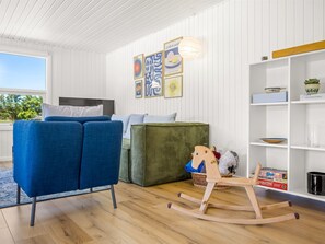 Een kamer met een blauwe bank, een groene poef, een houten schommelpaard en een plank met diverse spullen.