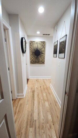 A hallway with wooden flooring, white walls, and a large abstract artwork. - Chic Bungalow in East Atlanta (Atlanta)