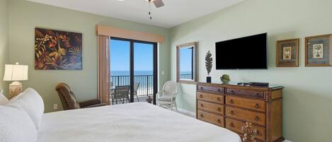 A hotel room with a large bed, a ceiling fan, a TV, a dresser, a chair, and a balcony with a view.