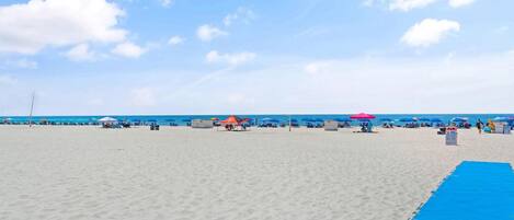 A beach with umbrellas and beach chairs, a blue mat, and a clear sky.