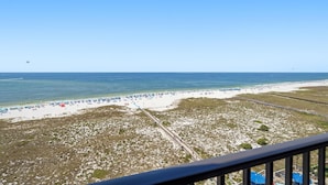 A beach with a clear sky, a sandy shore, and a few umbrellas. - Phoenix 6 1111 (Orange Beach)