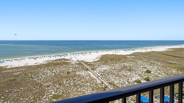 A beach with a clear sky, a sandy shore, and a few umbrellas. - Phoenix 6 1111 (Orange Beach)