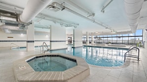 An indoor swimming pool with a hot tub, clear ceiling with ventilation ducts, and large windows providing natural light. - Phoenix 6 1111 (Orange Beach)