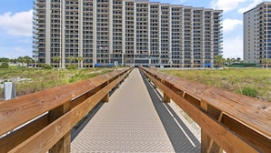 A long wooden boardwalk leading to a high-rise residential building with multiple balconies. - Phoenix 6 1111 (Orange Beach)