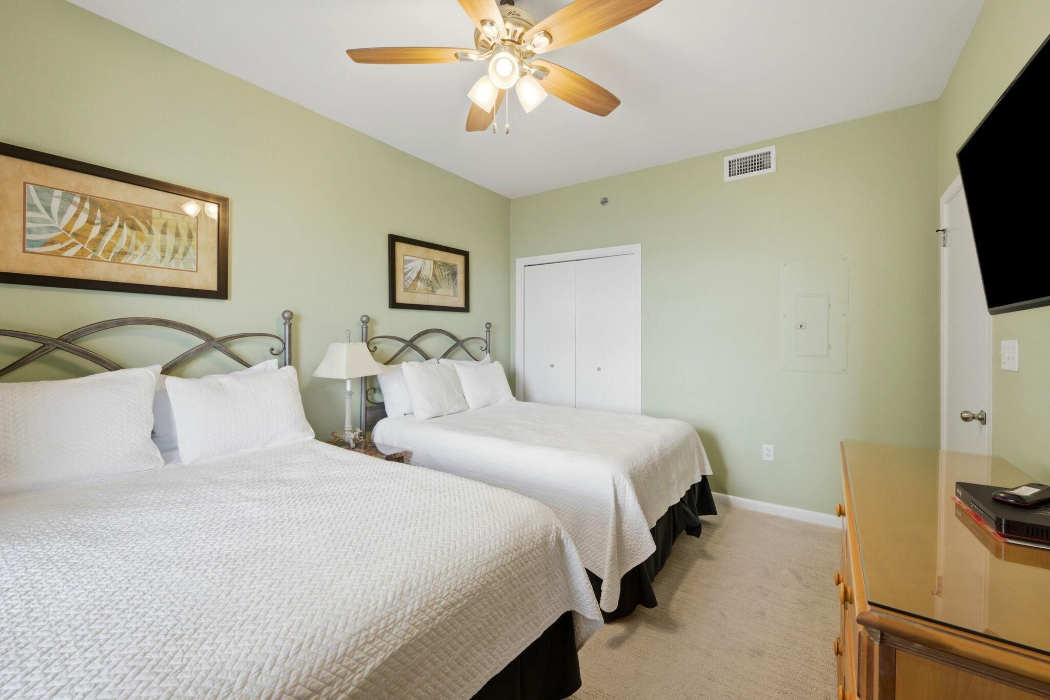 A bedroom with two beds, a ceiling fan, a dresser, and a TV.