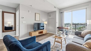 Ein modernes Wohnzimmer mit Flachbildfernseher, einer Couch, einem Couchtisch und einem großen Fenster mit Blick auf die Stadt.