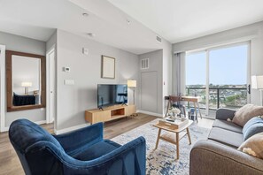 A modern living room with a flat-screen TV, a sofa, a coffee table, and a large window offering a city view. - Stamford Waterfront Retreat (Stamford, CT)