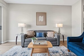A modern living room with a grey sofa, two side tables with lamps, a blue armchair, and a coffee table with a vase of flowers. - Stamford Waterfront Retreat (Stamford, CT)