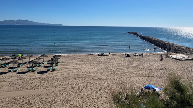 Une plage avec des parasols, des chaises longues et une digue rocheuse.