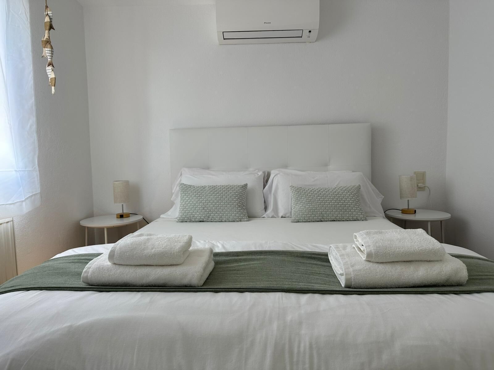 Habitación de hotel con una cama, dos mesitas de noche, aire acondicionado de pared y una ventana con cortinas.