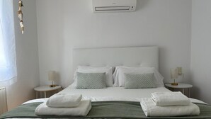 Une chambre d’hôtel comprenant un lit, deux tables de chevet, un climatiseur fixé au mur et une fenêtre avec des rideaux.