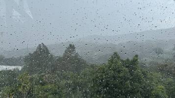 A view through a window with raindrops, a building, and trees.