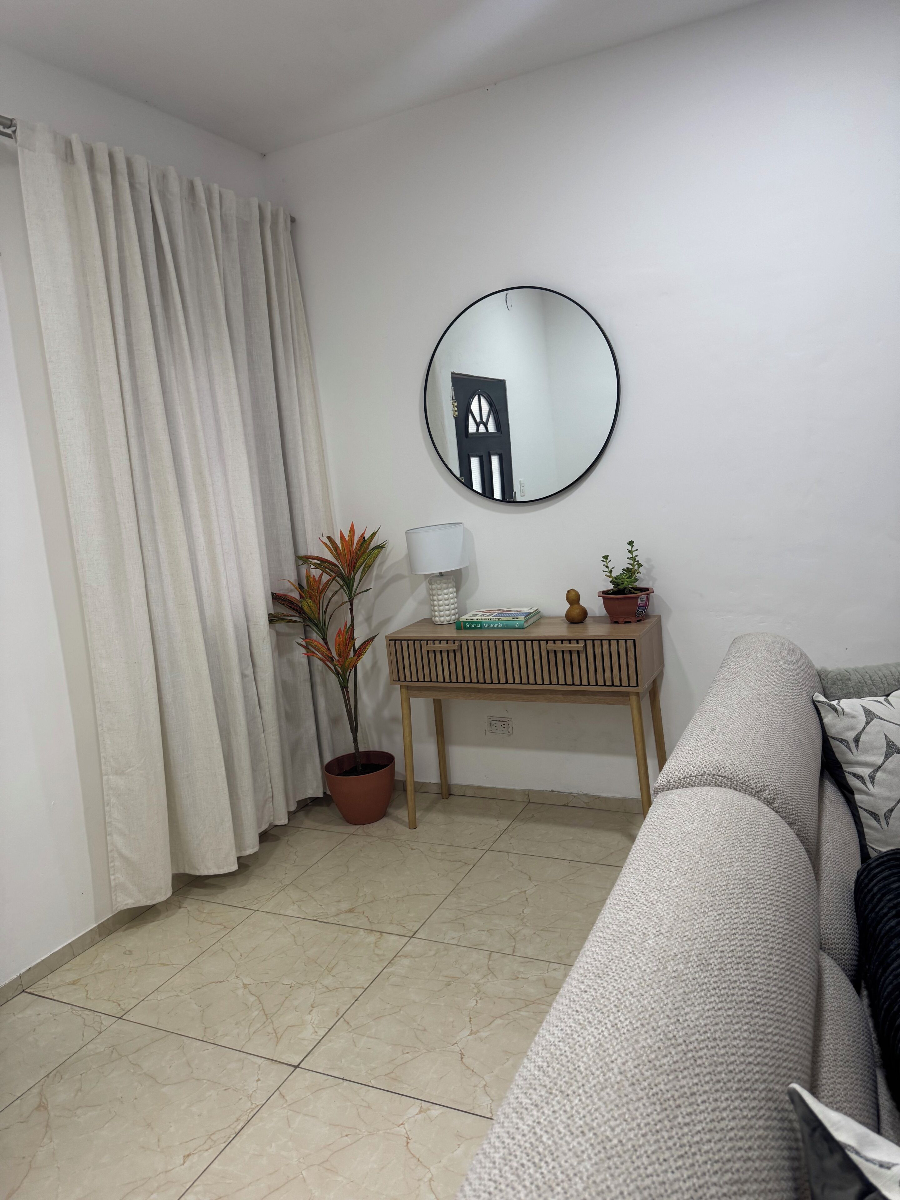 Un salon avec un canapé, un miroir rond, une petite table avec une lampe et une plante en pot.