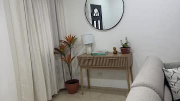 Un salon avec un canapé, un miroir rond, une petite table avec une lampe et une plante en pot.