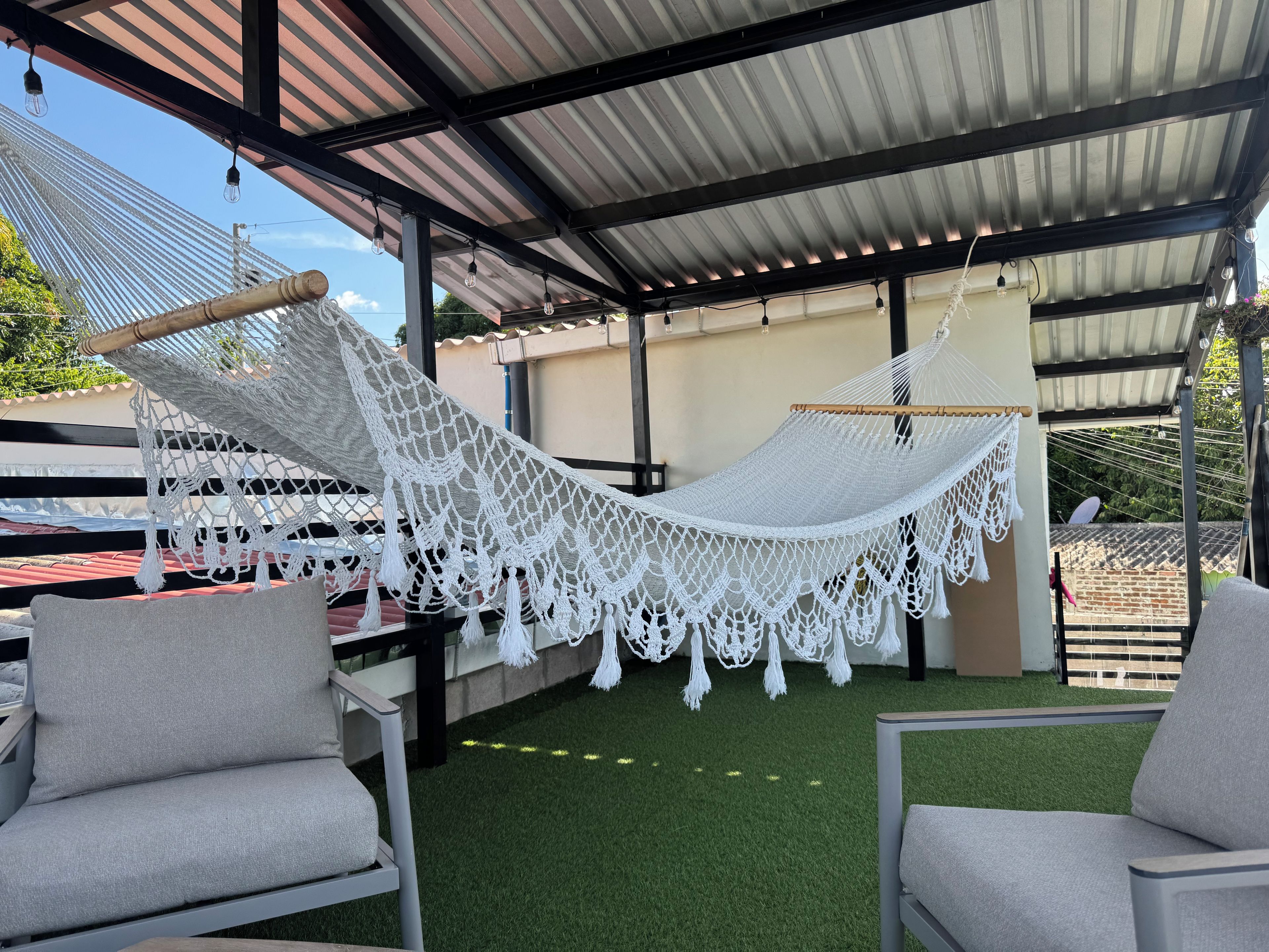 A hammock under a metal roof, two grey chairs, and artificial grass.