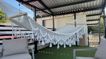 A hammock under a metal roof, two grey chairs, and artificial grass.