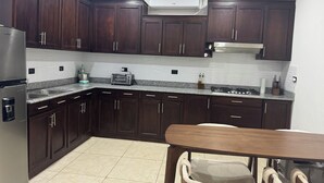 A modern kitchen with dark wood cabinets, a stainless steel refrigerator, a built-in oven, and a granite countertop.