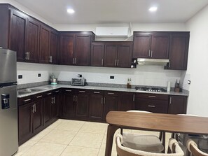 A modern kitchen with dark wood cabinets, a stainless steel refrigerator, a built-in oven, and a granite countertop.