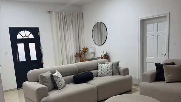 A living room with a beige sofa, a round ottoman, a mirror, and a door with a window.