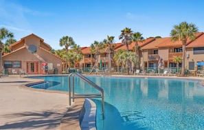 A hotel with a swimming pool, palm trees, and a clear blue sky. - Sandy Shores: Cozy 2-bedroom condo in pleasant Panama City Beach (Panama City Beach)