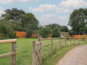 Ländliche Szenerie mit Holzzaun, Kiesweg und zwei Holzhäusern mit Anbauten.
