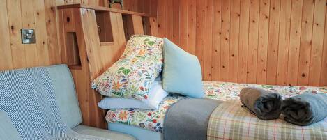 Interior de una cabaña de madera con una cama, una silla, una ventana y una repisa con una figurita de venado.