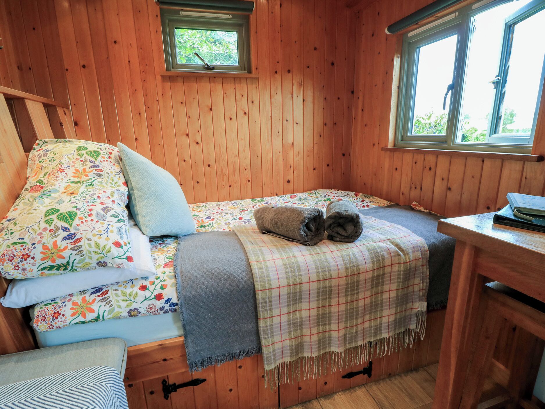 A wooden cabin room with a bed, a small table, and a window.