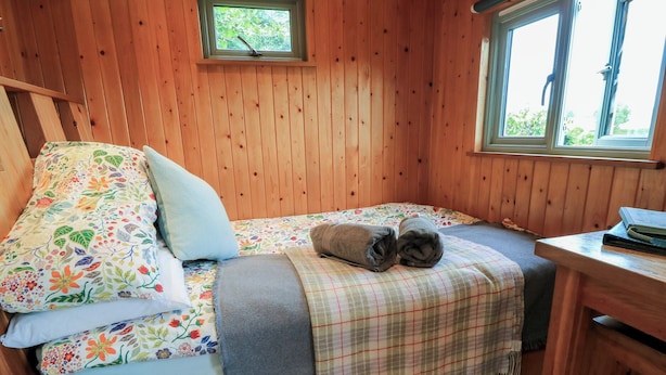A wooden cabin room with a bed, a small table, and a window. - Pippins (Taunton)